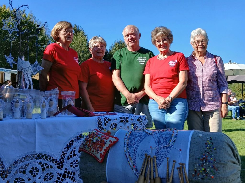 Fünf Vereinsmitglieder in Vereins-T-Shirts hinter der Klöppelrolle mit Klöppelbrief