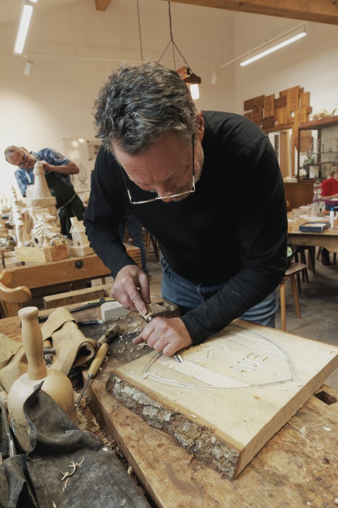 Vereinsmitglied schnitzt ein Wappen in eine Holztafel mit Rinde am Rand
